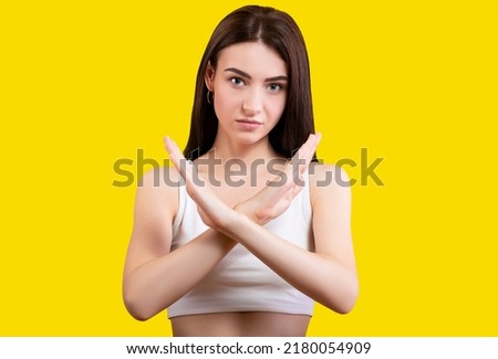 Attractive cute girl folded says stop in a white top on a yellow background. Shows stop