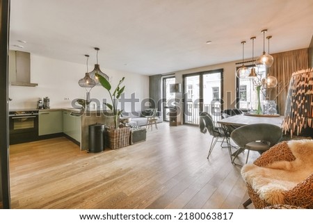Interior of spacious light dining room and elegant chandelier located near kitchen with modern furniture and appliances Royalty-Free Stock Photo #2180063817