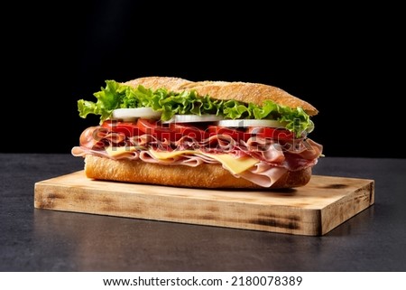 Submarine sandwich with ham, cheese, lettuce, tomatoes,onion, mortadella and sausage on wooden table Royalty-Free Stock Photo #2180078389