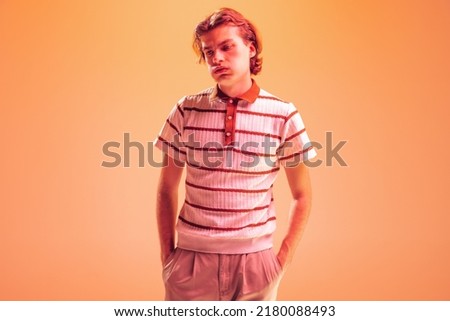 Portrait of young man posing isolated over orange studio backgorund in neon light. Looks tired, exhausted. Overworking. Concept of youth, fashion, lifestyle, emotions. Copy space for ad