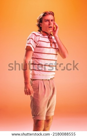 Portrait of young emotive man posing with shocked facial expression isolated over orange background in neon light. Expressive news. Concept of youth, fashion, lifestyle, emotions. Copy space for ad