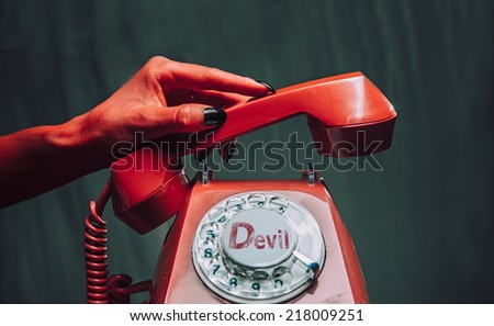 Red devil hand hangs up the handset on retro phone on dark background. Halloween or horror theme