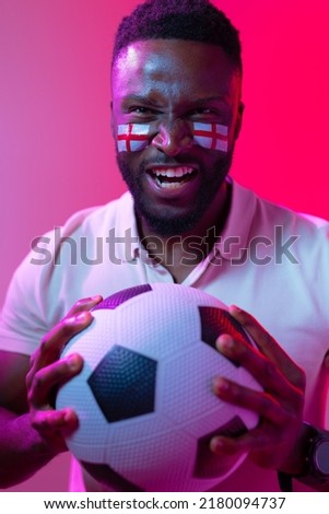 Vertical image of african american male soccer fan with flag of england in neon pink lighting. Sport, fans, cheering and emotions concept.