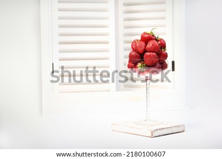 Strawberries in a tall elegant wine glass. A white window with shutters in the background. Summer season. Space for copying.White background.