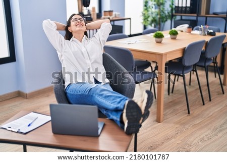 Young hispanic woman business worker relaxed with hands on head at office