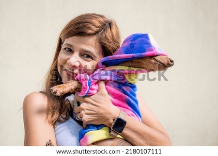 Latin woman holding her dog both dressed alike.  She is looking at camera.