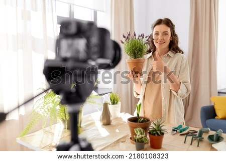 blogging, gardening and housework concept - happy woman or blogger with camera and pot flowers recording tutorial video and showing thumbs up at home