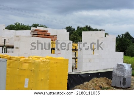 A house under construction, walls made of acc blocks, rough windows and door openings, reinforced brick lintels, a scaffolding, insulated foundation walls, solid concrete blocks and acc blocks Royalty-Free Stock Photo #2180111035