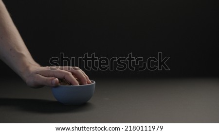 man take roasted salted pistachios from blue bowl on black paper background