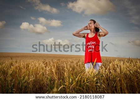 woman standing in a field listening to music on headphones, positive vibes only t shirt.