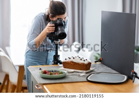 blogging, profession and people concept - female food photographer with camera photographing cake in kitchen at home Royalty-Free Stock Photo #2180119155