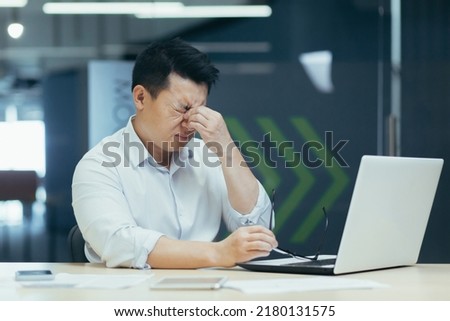 Tired Asian businessman working late in office, sore eyes, man with laptop Royalty-Free Stock Photo #2180131575