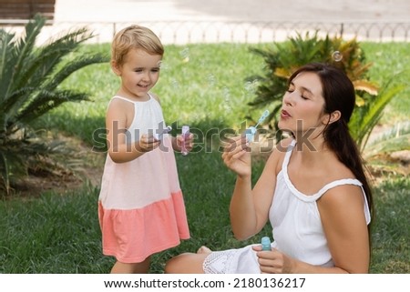 Positive kid holding soap bubbles near mother on lawn