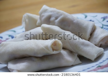 Heap of raw spring rolls(lumpia) on the plate. Frozen food on wooden tables.
