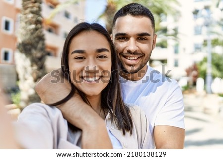 Young latin couple smiling happy and hugging making selfie by the camera at the city.