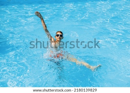 Little Boy in sunglasses swims in the pool, smiling and having a happy day. Cute happy little boy swims and dives in the pool on a sunny day. Vacation, summer, vacation