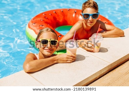 Beautiful little girl and friend boy in sunglasses, with fresh cocktails have fun in the pool on a sunny summer day, Happy friends with drinks at summer pool party. Summer vacation concept