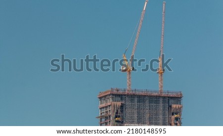 High multi-storey building under construction and many cranes timelapse. Active work at construction site of new skyscraper with blue sky on a background.
