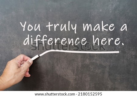 Male hand writes in white chalk pencil the word you truly make a difference here a chalkboard background. Encouragement words.