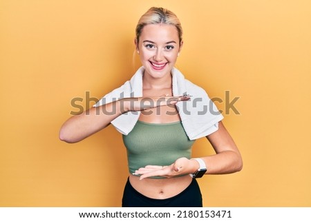 Young blonde girl wearing sportswear and towel gesturing with hands showing big and large size sign, measure symbol. smiling looking at the camera. measuring concept. 