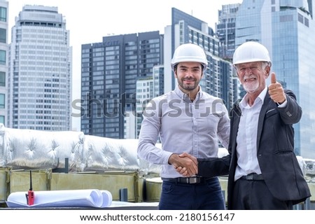 Caucasian engineer or architect with safety helmet handshake for good deal with blueprints for inspection details on construction site and building background.
