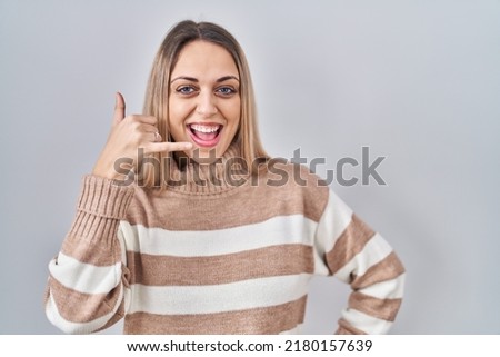 Young blonde woman wearing turtleneck sweater over isolated background smiling doing phone gesture with hand and fingers like talking on the telephone. communicating concepts. 