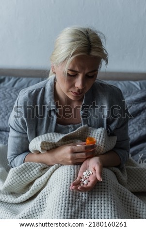 sad woman with climax sitting in bed and looking at bottle with painkillers Royalty-Free Stock Photo #2180160261