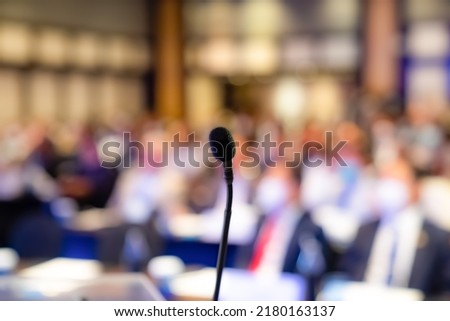 Small microphone behind the podium for the MC, master of ceremony, with a blurry crowd audience in the background in a seminar.