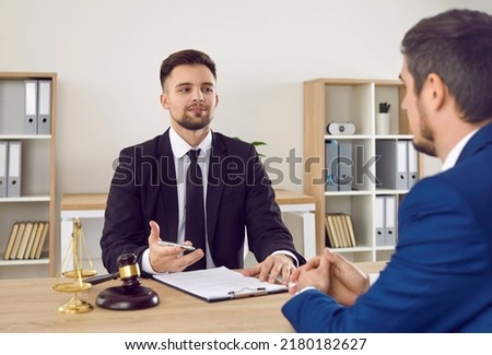 Lawyer having a meeting with a new client. Young male attorney in suit and tie sitting at office desk, sharing legal advice, explaining inheritance process, trying to help. Law consultation concept Royalty-Free Stock Photo #2180182627