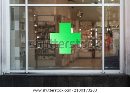 Green cross sign with neon light mounted on pharmacy shop window case outdoor