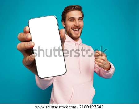 Mobile App Advertisement. Handsome Excited Man Showing Pointing At Empty Smartphone Screen Posing Over Light Blue Studio Background, Smiling To Camera. Check This Out, Cellphone Display Mock Up Royalty-Free Stock Photo #2180197543