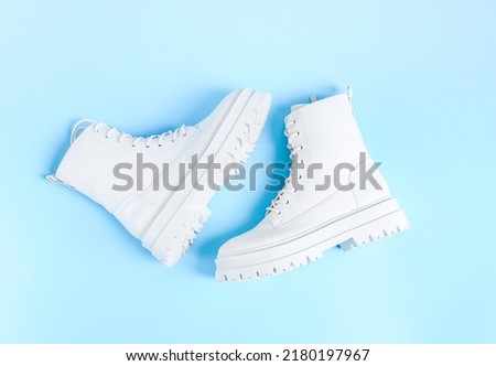 White demi-season martens boots made of eco-leather with a rough sole lie in the center on a light blue background, flat lay close-up. The concept of women's shoes. Royalty-Free Stock Photo #2180197967