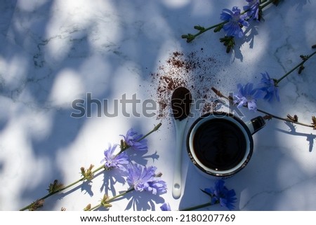 Cup of coffee with blue chicory flower on marble table in sunlight. Plant shadows. Top view, flat lay, copy space. Healthy eating concept. Healthy herbal alternative coffee surrogate
