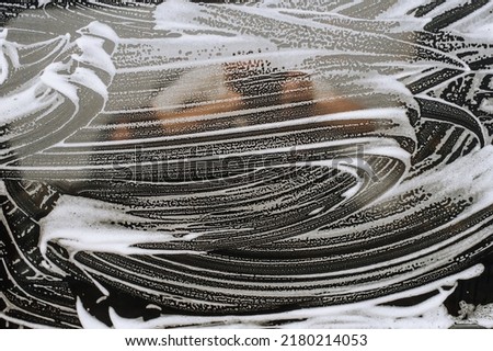 Background, texture of the black surface of a metal door, car windows in white soapy foam after washing. Photography, shampoo pattern concept, copy space.