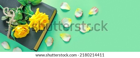 Beautiful bouquet of yellow roses with vintage book and flower petals on green table. Home office and sheet of paper for holiday invitation or congratulations.
Flat lay, top view, copy space concept.