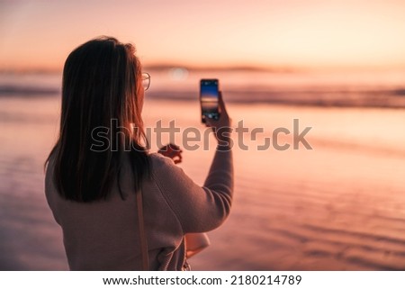 silhouette portrait of a woman on the beach at sunset taking a picture with the cell phone