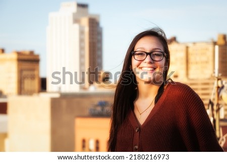 portrait of a pretty teenaged girl with dark hair and glasses with city skyline Royalty-Free Stock Photo #2180216973