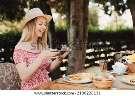 Young woman taking photos of food in a restaurant with a smartphone during summer day