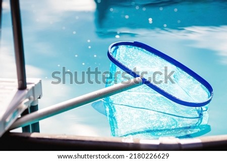 Cleaning a swimming pool with a metal frame with a net from leaves and dirt. Pool cleaner during work. Solar banner. The concept of summer holidays.
