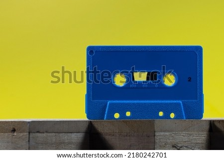 A blue audio cassette on a wood surface against a yellow background in a studio environment