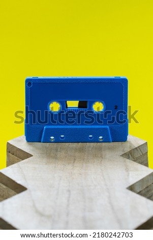 A blue audio cassette on a wood surface against a bright yellow background in a studio environment