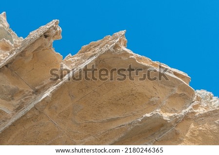 Large rock of yellow and orange color against blue sky. Texture background of rock and sky.