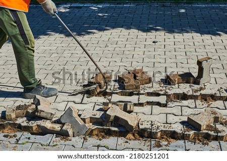 Replacement of paving slabs. Workers remove old tiles with a metal hook