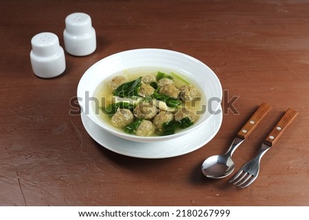 Sop Bakso is a clear soup made from a mixture of meatballs and vegetables (green mustard), seasoned with pepper, garlic, scallions and celery. Served in a bowl on the table. Selective focus