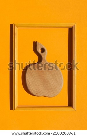 Cutting board in the shape of an apple in a rectangular wooden frame on an orange background. Decoration of a cafe, restaurant