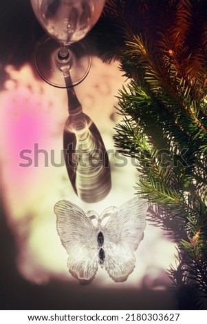 Blurred shadow of wine glass with light passes through glass.  branch of Christmas tree and christmas butterfly toy . Abstract, play of light and shadow, shadow play illusion . Christmas still life