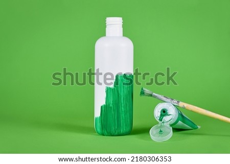 Greenwashing concept with white plastic bottle being painted green Royalty-Free Stock Photo #2180306353