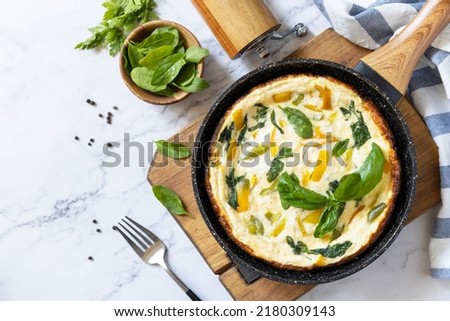 Spinach and cheese omelette. Frittata made of eggs, paprika and spinach in a frying pan on a marble countertop. View from above. Copy space. Royalty-Free Stock Photo #2180309143