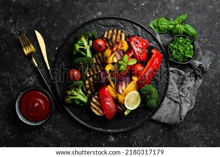 Grilled vegetables (colorful bell pepper, zucchini, eggplant, cherry tomatoes and broccoli) on a black stone plate. Top view. Rustic style. Royalty-Free Stock Photo #2180317179