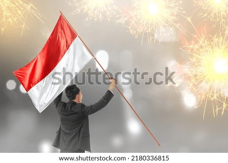 Rear view of Asian businessman holding an Indonesian flag with a fireworks background. Indonesian independence day